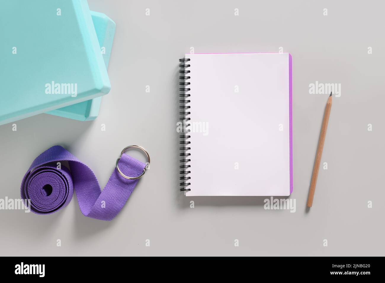 Green yoga blocks, violet belt and notebook on gray background. Training plan. Workouts plan. Stock Photo