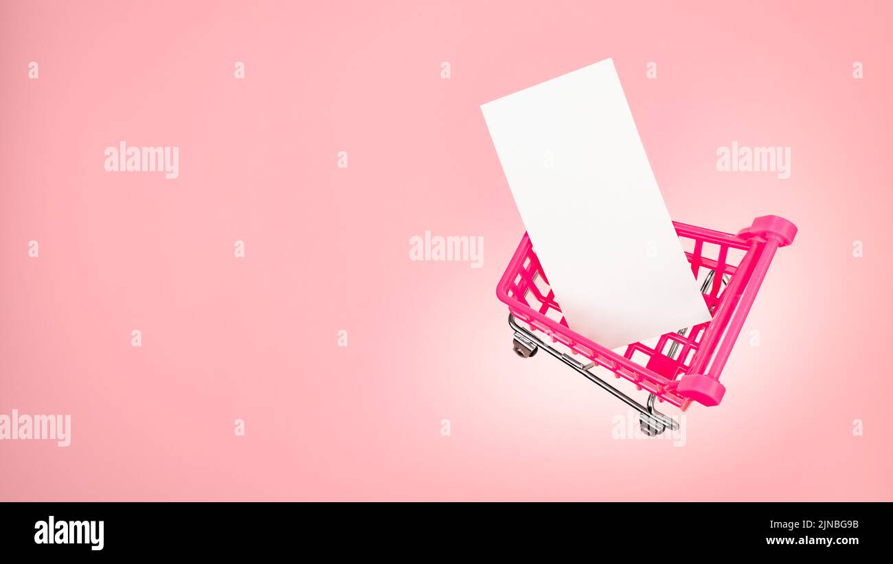 Small shopping cart market trolley with blank paper tag label white blank paper on pink background. Pink sale cart is clear message card blank. Pink Stock Photo