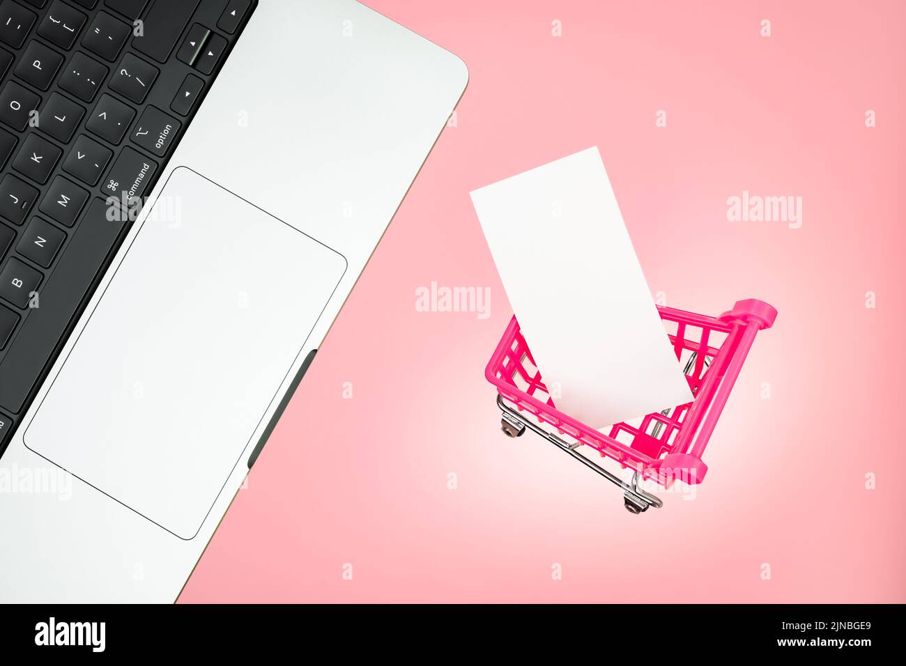 Laptop shopping cart with blank paper tag label white blank paper on pink background. Laptop pink shopping concept. Keyboard laptop cart sale online Stock Photo