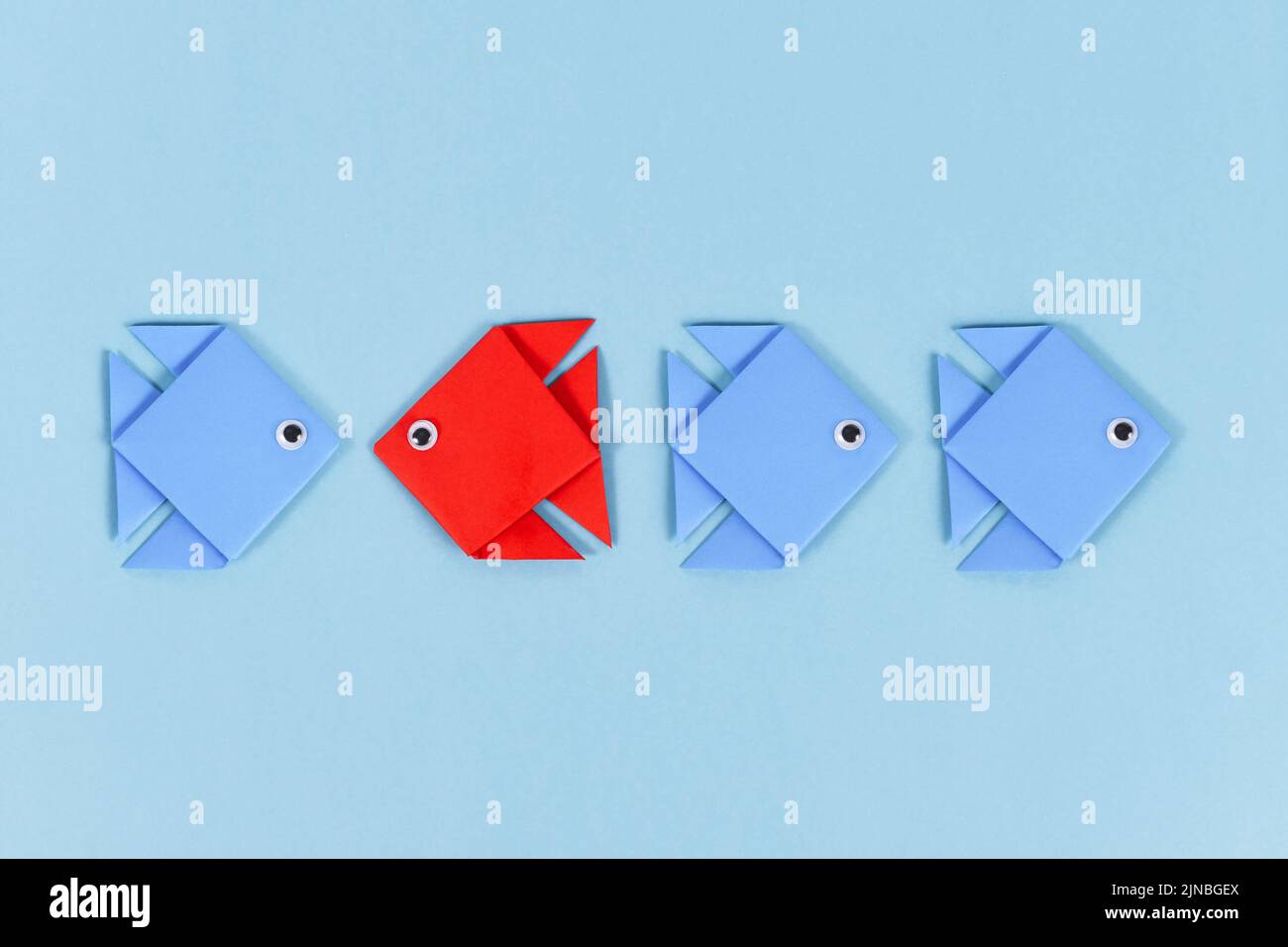 Red paper fish swimming swimming against the current in opposite direction of blue fish Stock Photo