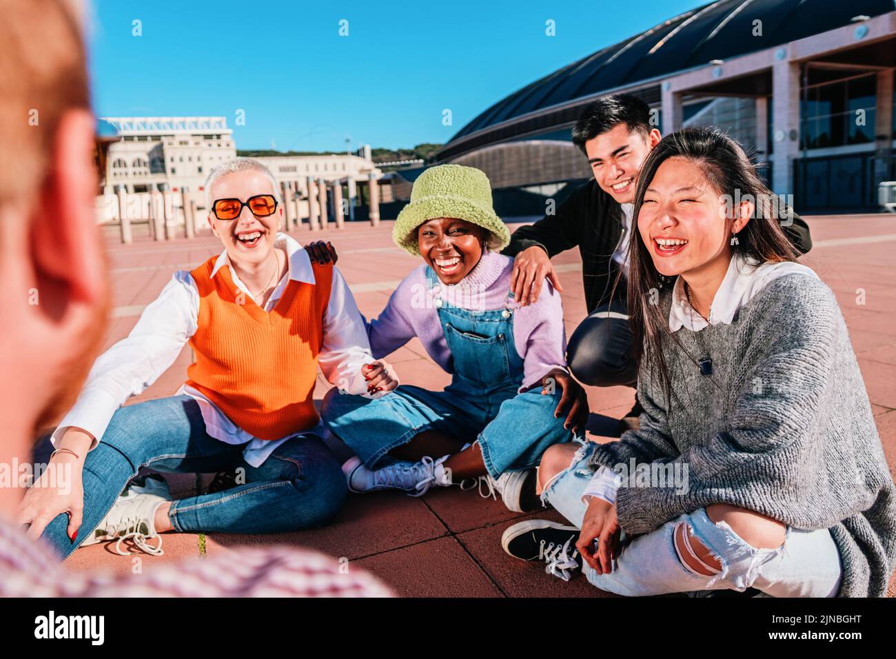 Group of diverse friends laughing and talking sitting on the floor outdoors. Stock Photo