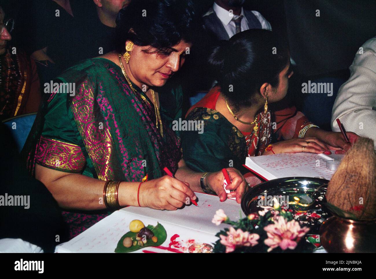 Women Writing with Red Pen in the Red Chopdis Performing Chopda Puja During Diwali Signifying the Start of the new Stock Photo