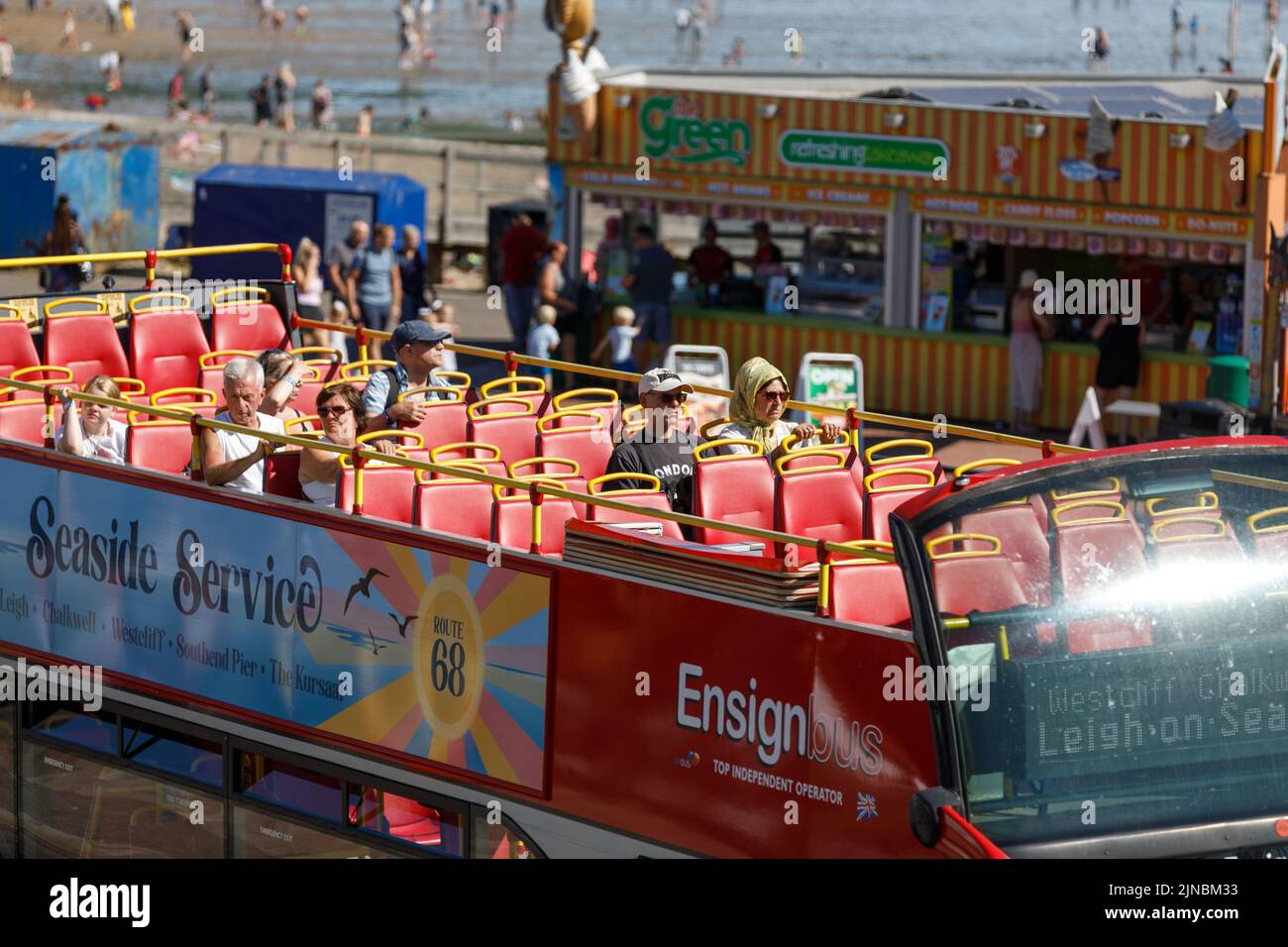 Open top bus, top deck with passengers, on a beachfront road at the English seaside in Essex, England. Red bus, close up, from above, sunny, bright Stock Photo