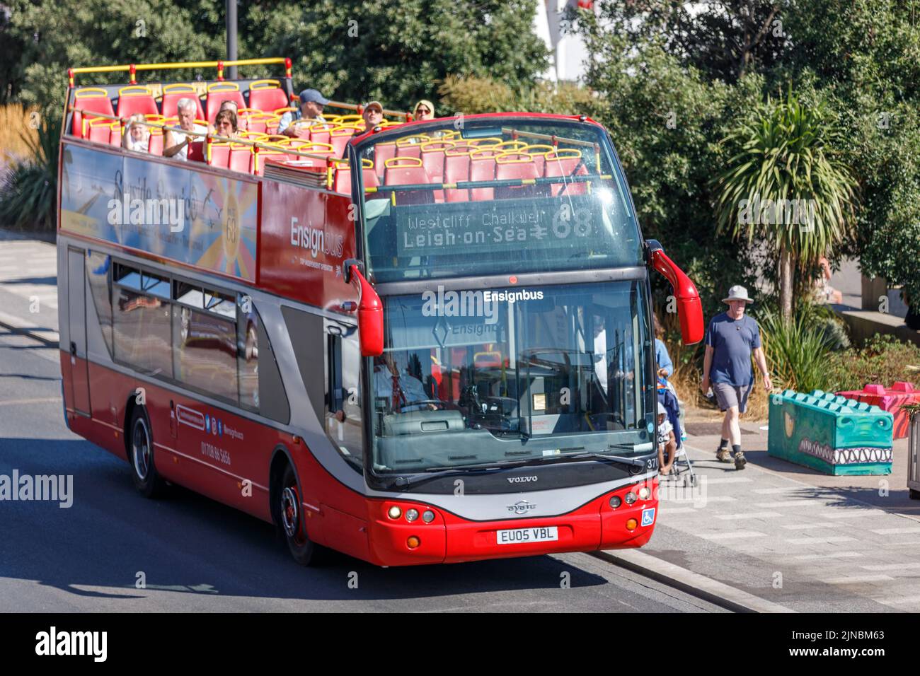 Red Bus with open top on a seaside sightseeing tour at Southend Beach, Marine Parade with passenger on the top deck and tourists walking the pavement Stock Photo