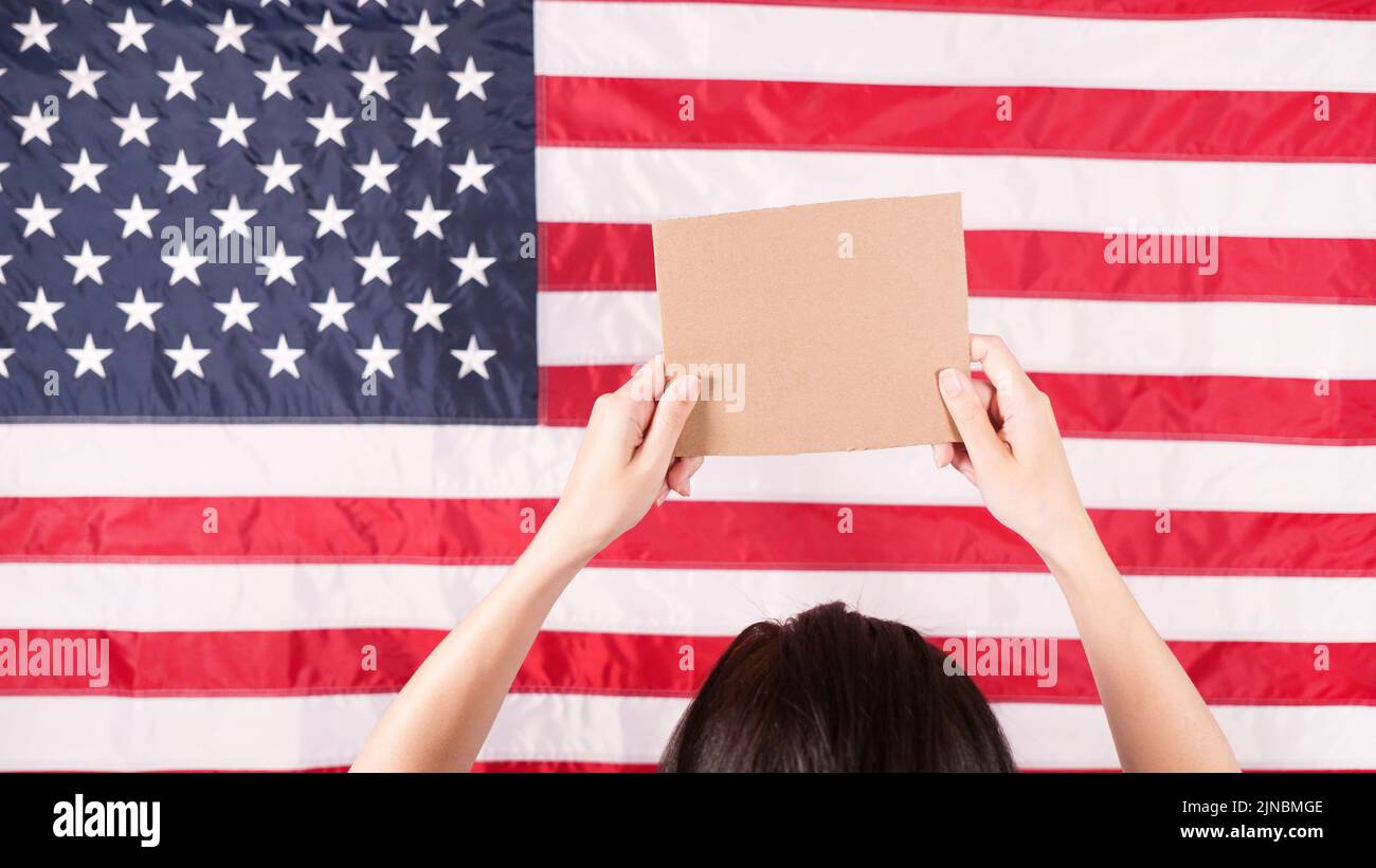 Woman is holding an empty cardboard with Space for Text sign US flag on background. Protest against anti abortion law. Women's strike. Womens rights Stock Photo