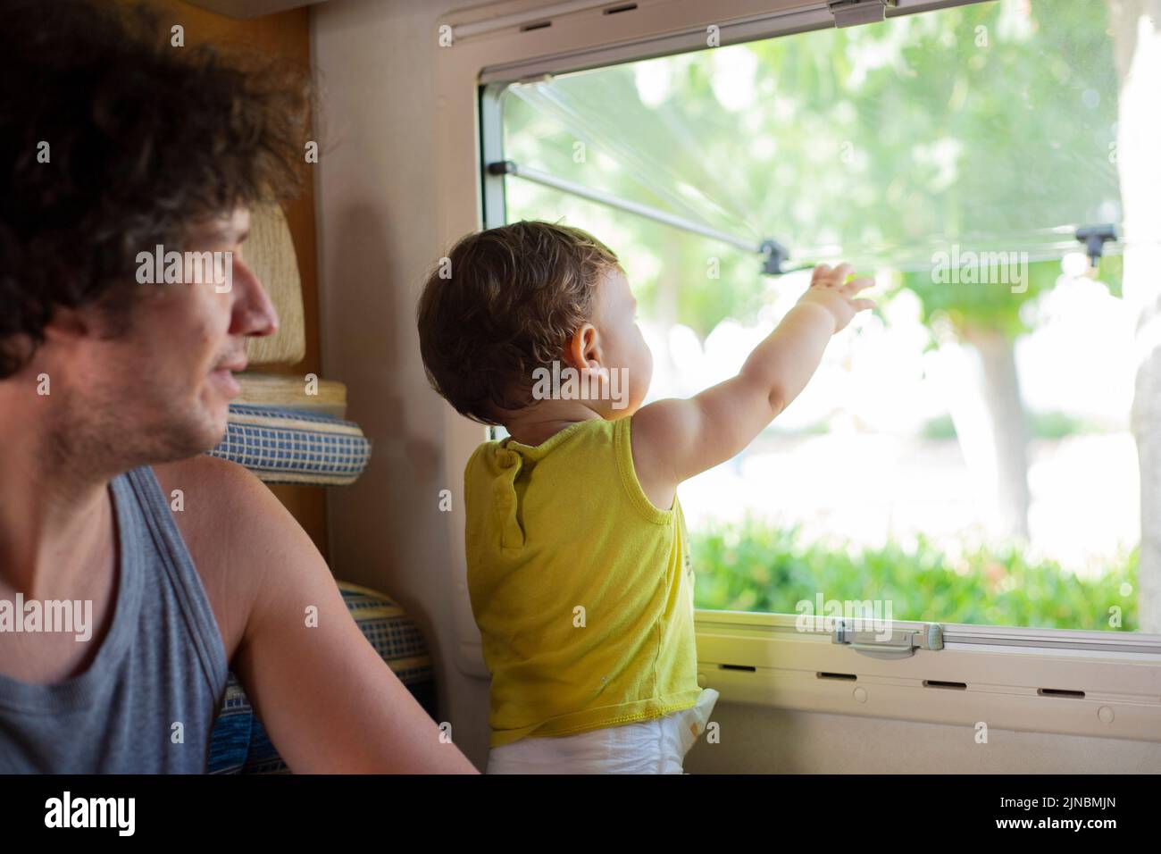 Young caucasian father and toddler child looking out of a window in a motorhome or campervan. Travel with children in camper. Stock Photo