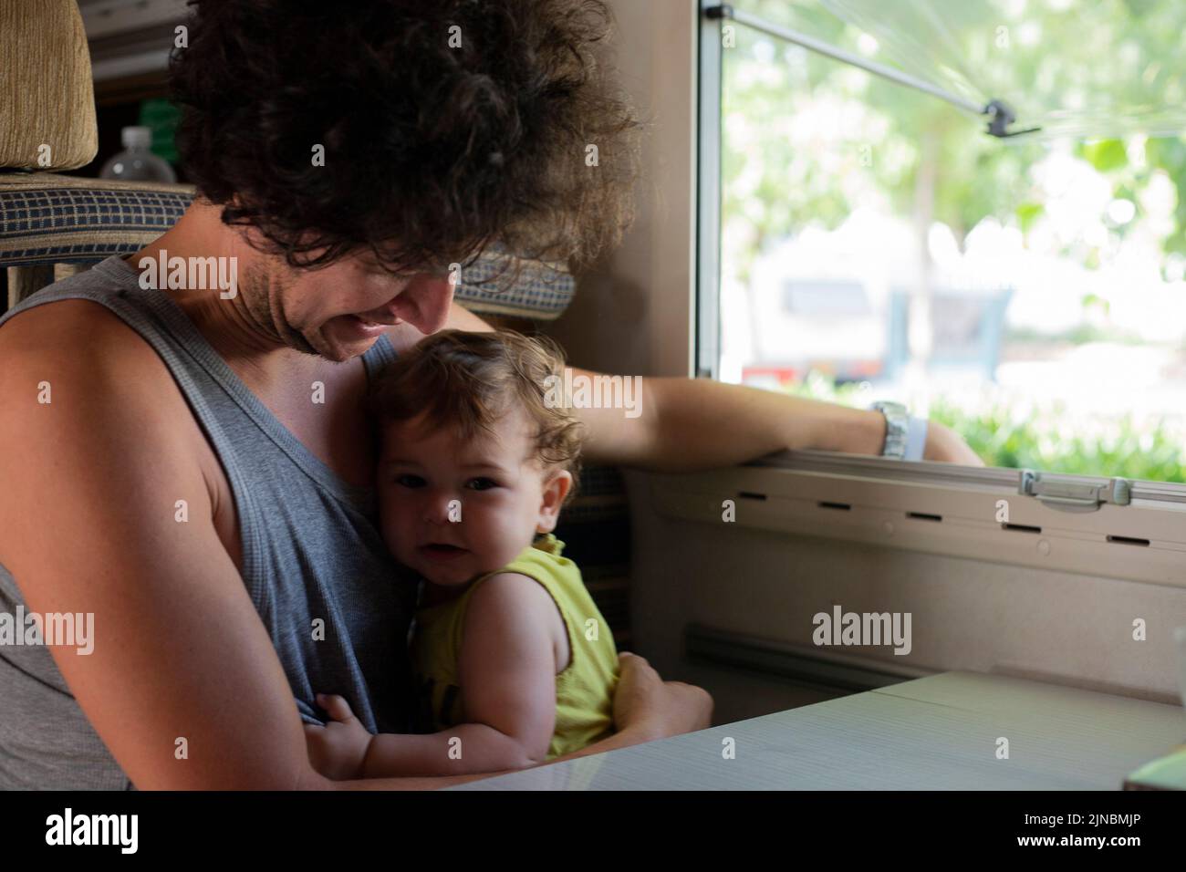 Young caucasian father and toddler child cuddling and embracing in a motorhome or campervan. Travel with children in camper. Stock Photo