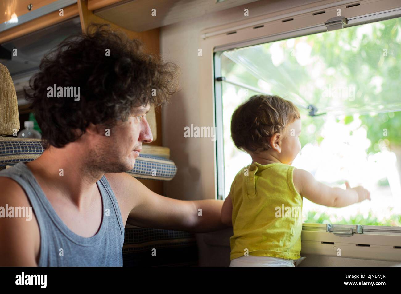 Young caucasian father and toddler child looking out of a window in a motorhome or campervan. Travel with children in camper. Stock Photo