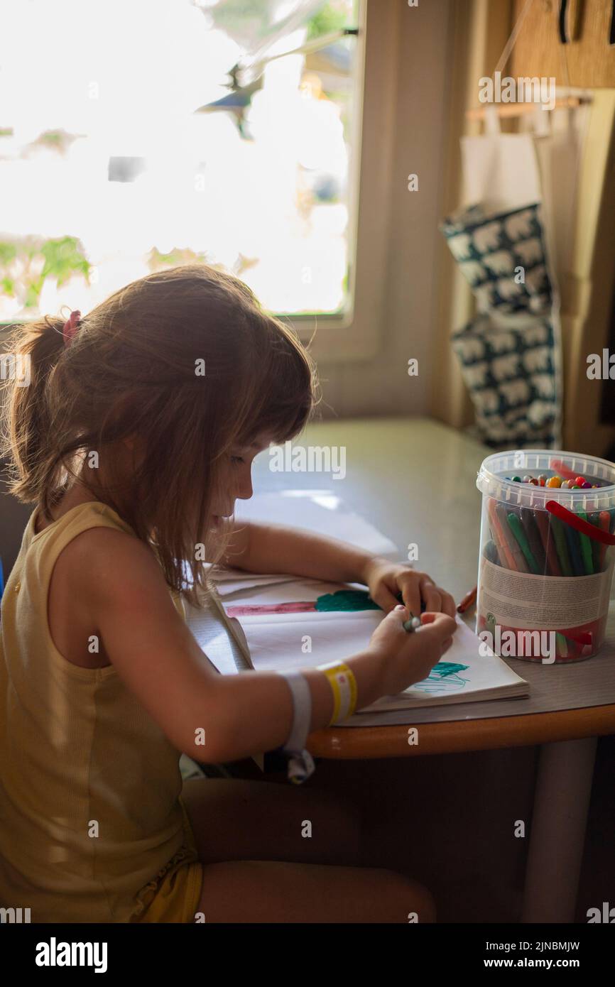 Caucasian child girl drawing with markers in a motorhome or campervan. Travel with children in camper. Vertical portrait. Stock Photo