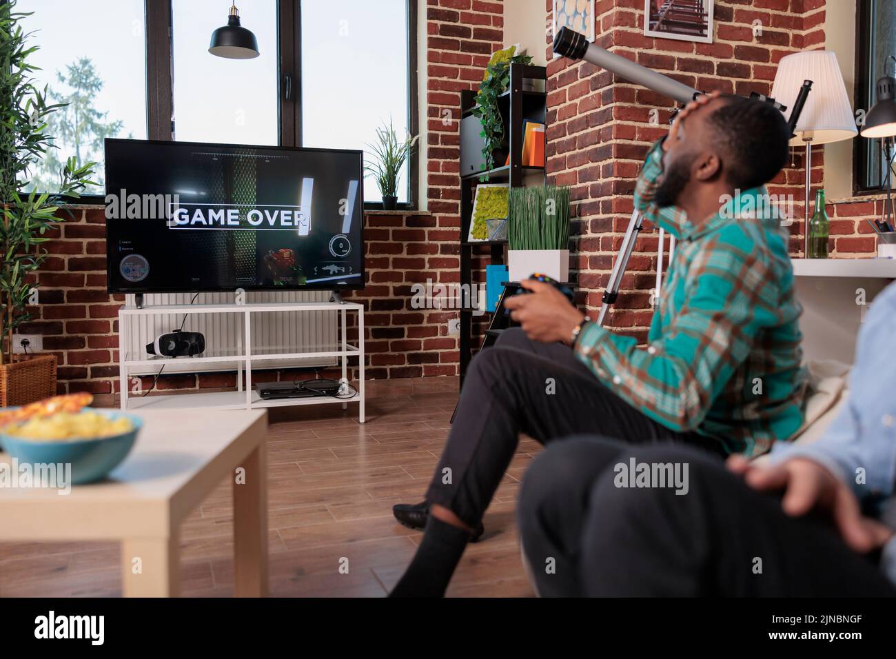 Young adult feeling frustrated about lost video games competition, playing shooting game on tv console and losing. Sad man being angry after gaming strategy lose, relaxing with friends. Stock Photo