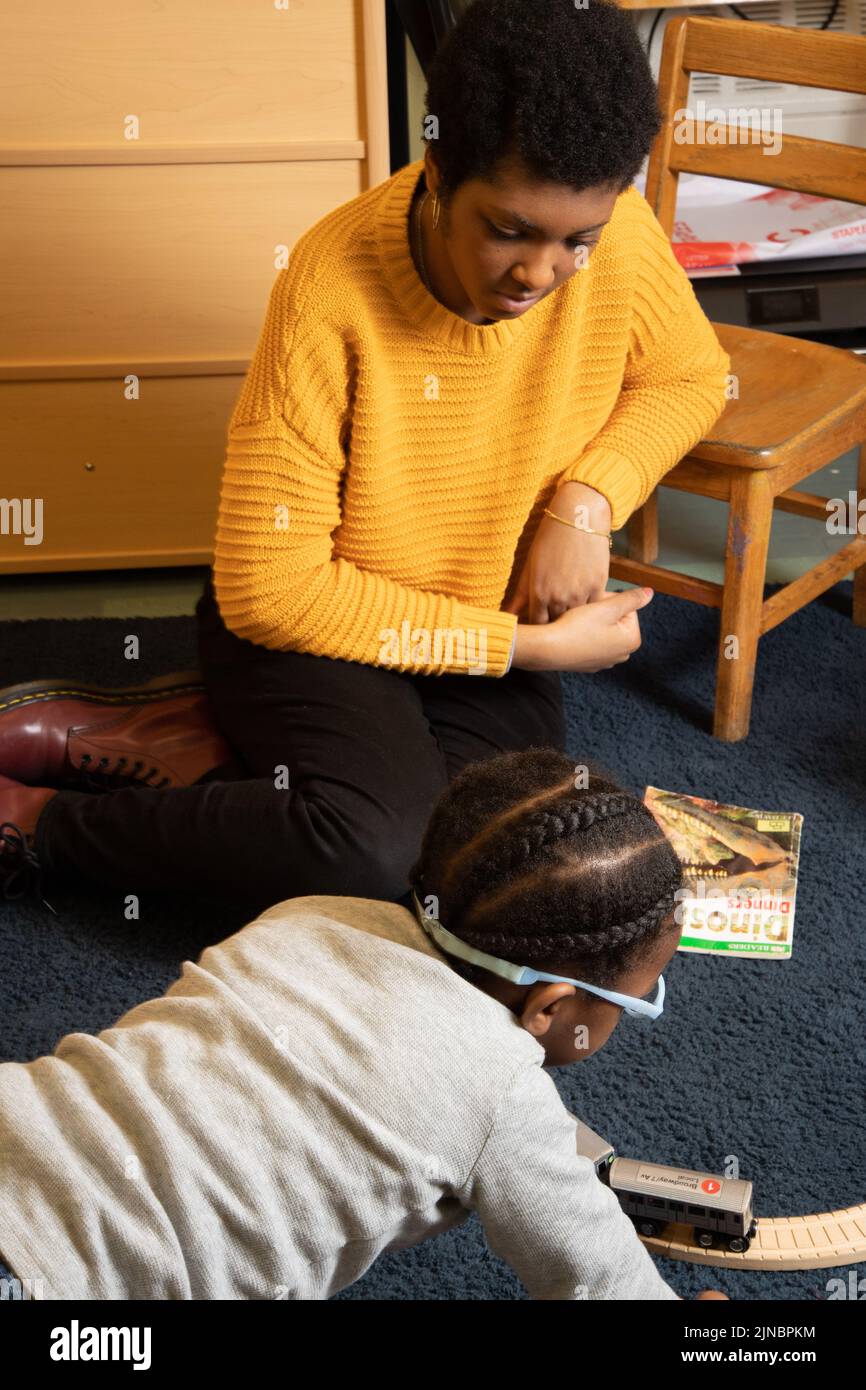 Education Preschool Child Care 2-3 year olds female teacher watching boy play with train set, on floor with him Stock Photo