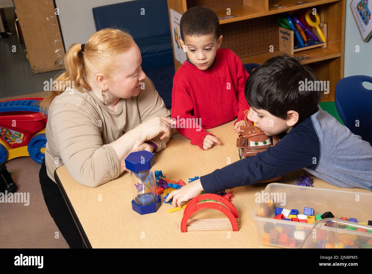 Education Preschool Child Care 3 year olds two boys conflict over toy, teacher working with children to resolve conflict, using timer to structure tim Stock Photo