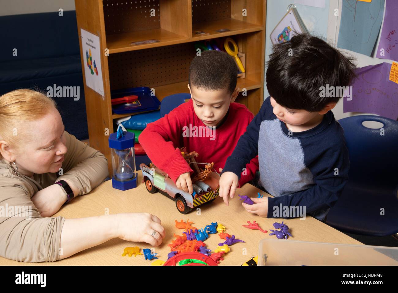 Education Preschool Child Care 3 year olds two boys conflict over toy, teacher working with children to resolve conflict, boys play together with toy Stock Photo