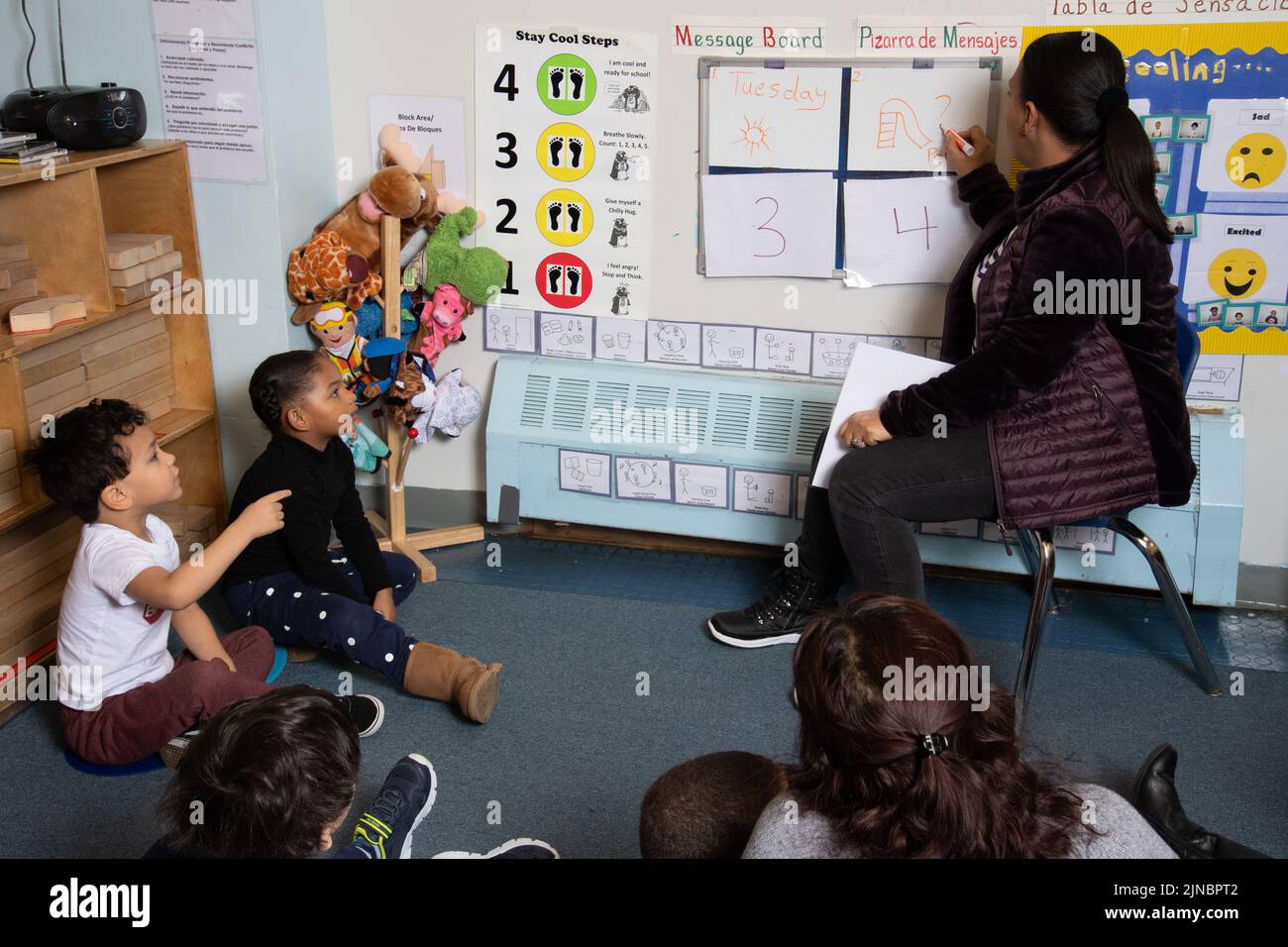 Education Preschool Child Care 3 year olds group with female teachers at meeting time, message board signs in English and Spanish Stock Photo