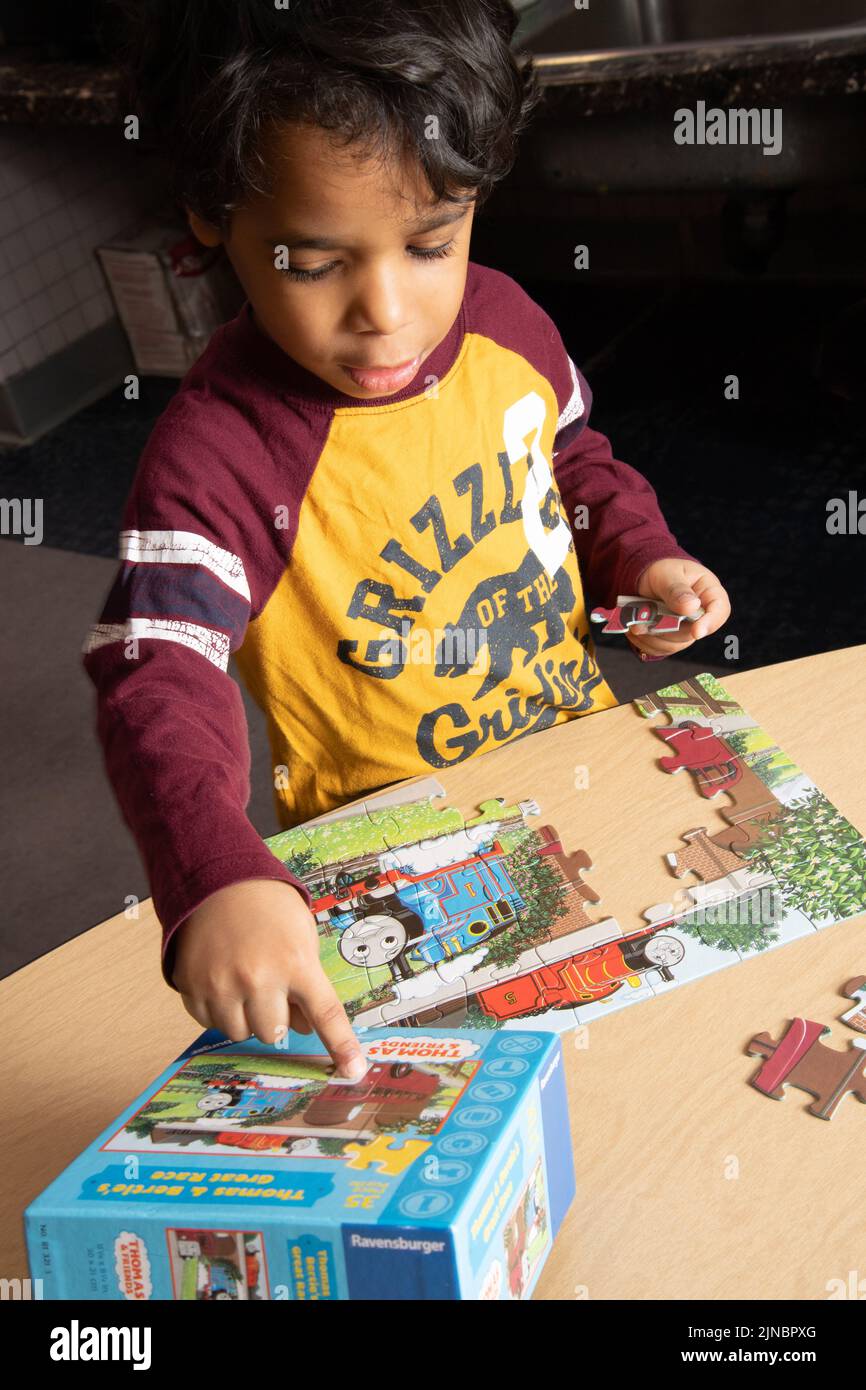 Education preschool 4 year olds boy doing jigsaw puzzle, using illustration on box to assist him Stock Photo