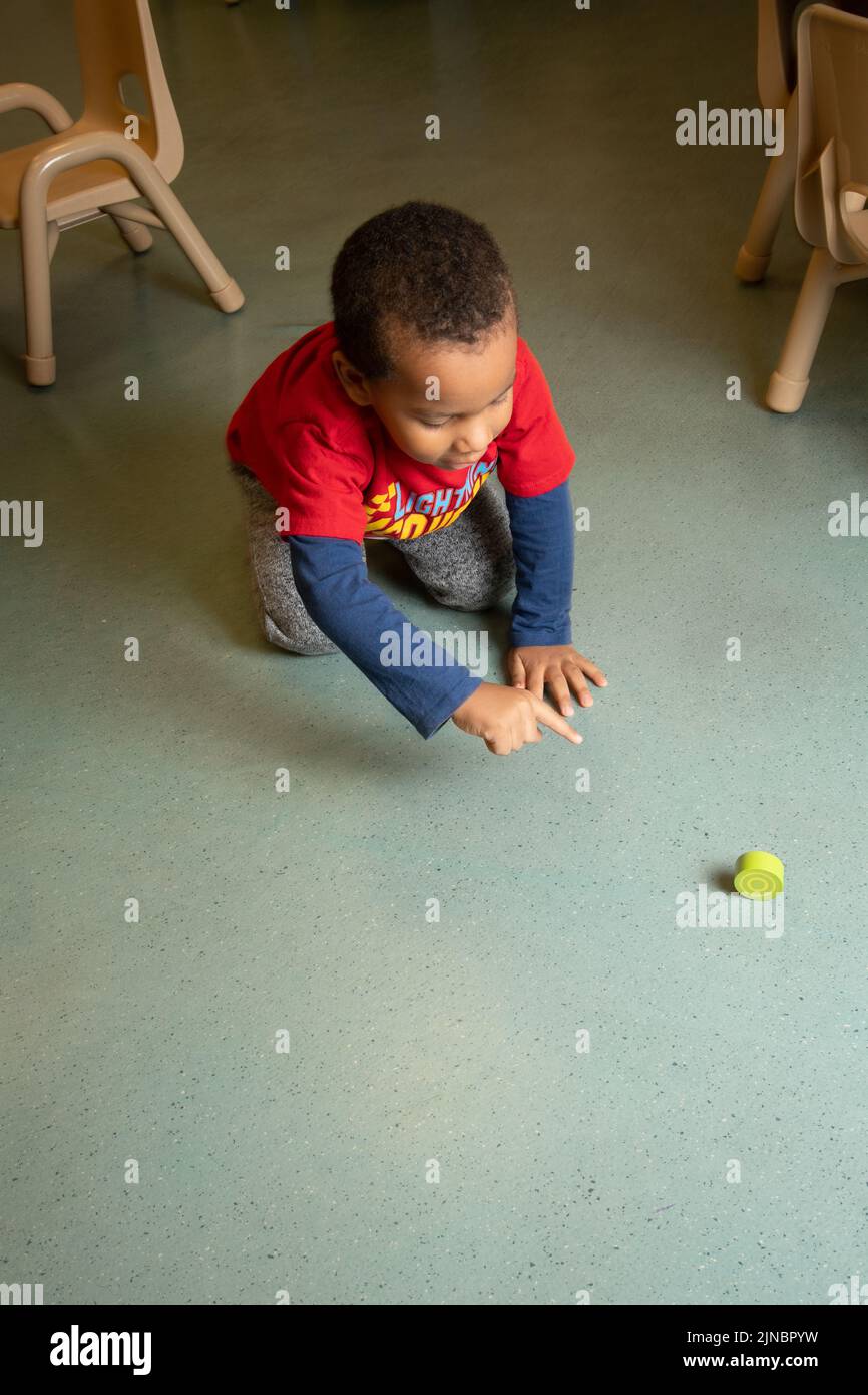 Education Preschool Child Care 2-3 year olds boy rolling round block excited to watch it roll, pointing at it Stock Photo