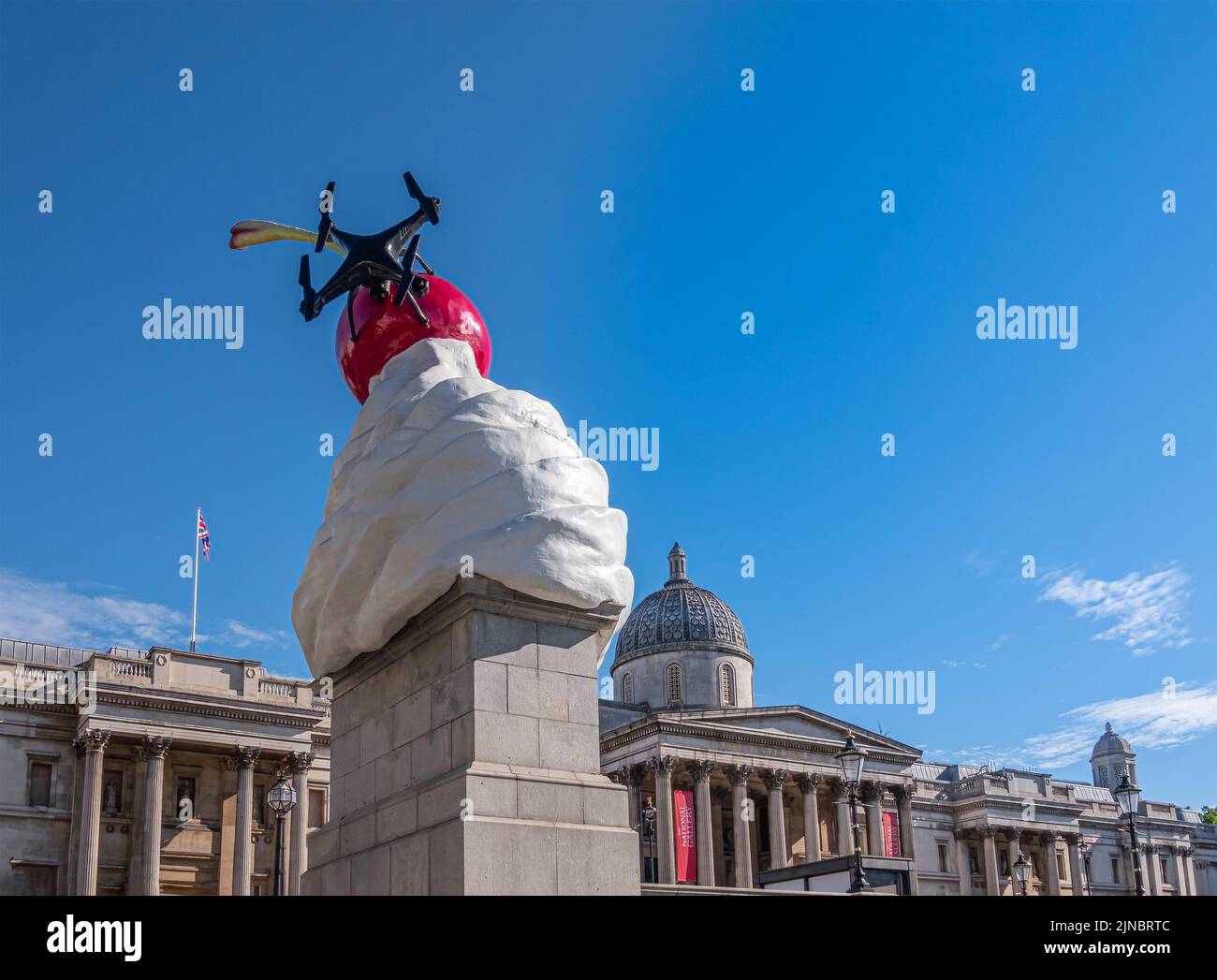 London, UK- July 4, 2022: Trafalgar Square. Whipped Cream With red Cherry on top statue, named The End, against blue sky. Drone part of statue. Nation Stock Photo