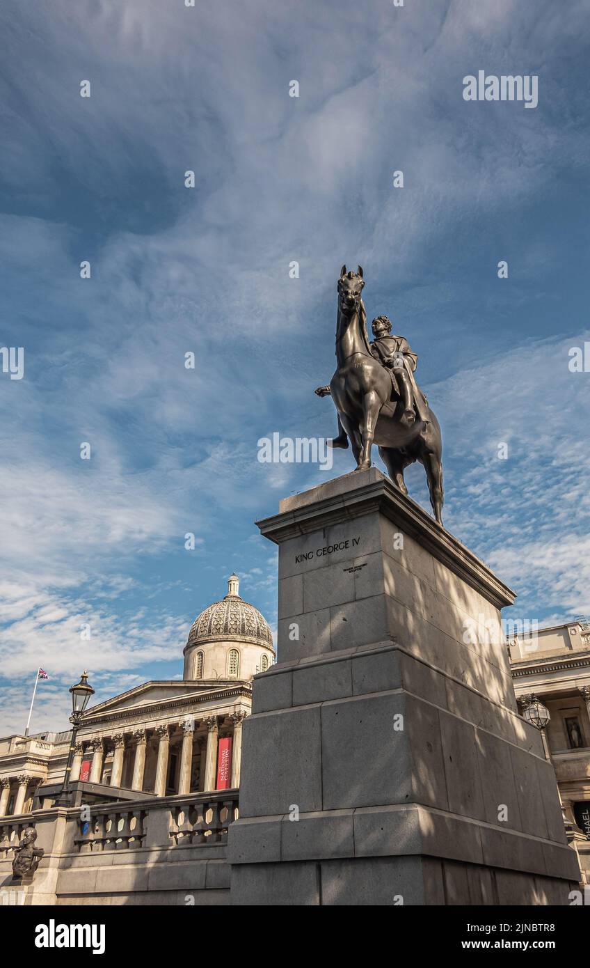 London, UK- July 4, 2022: Trafalgar Square. King George IV on his horse statue and pedestal with Nationl Gallery facade in back under blue cloudscape. Stock Photo