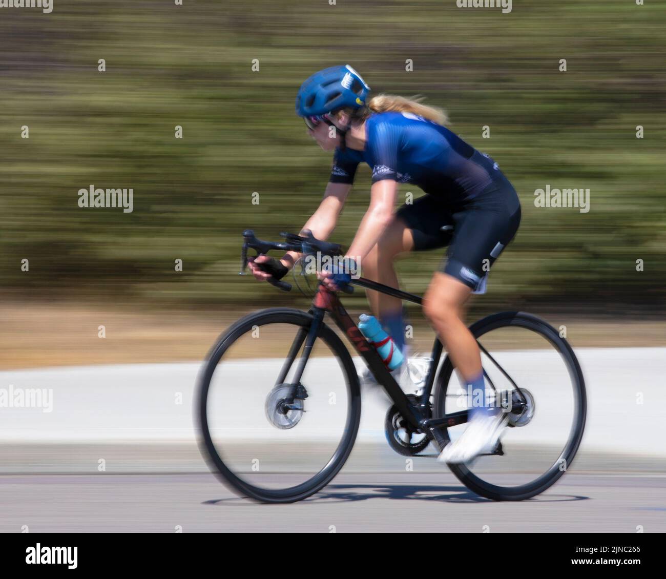 Female cyclist in the lead riding her bike on a lap of a Criterium, a fast cycling race around repeated short circuits on city streets. Motion blur. Stock Photo