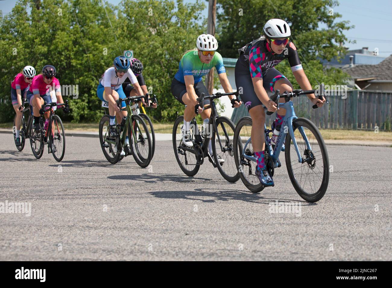 Female bicycle racers riding a lap of a Criterium, a cycling race where the women ride their bikes around a circuit on city streets. Stock Photo