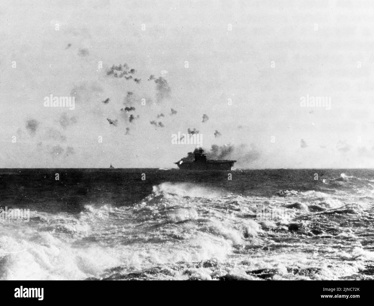 The carrier USS Enterprise manoeuvring under aerial attack during the Battle of the Eastern Solomons. The fire on the left of the ship is a gun battery burning after a bomb hit. Stock Photo