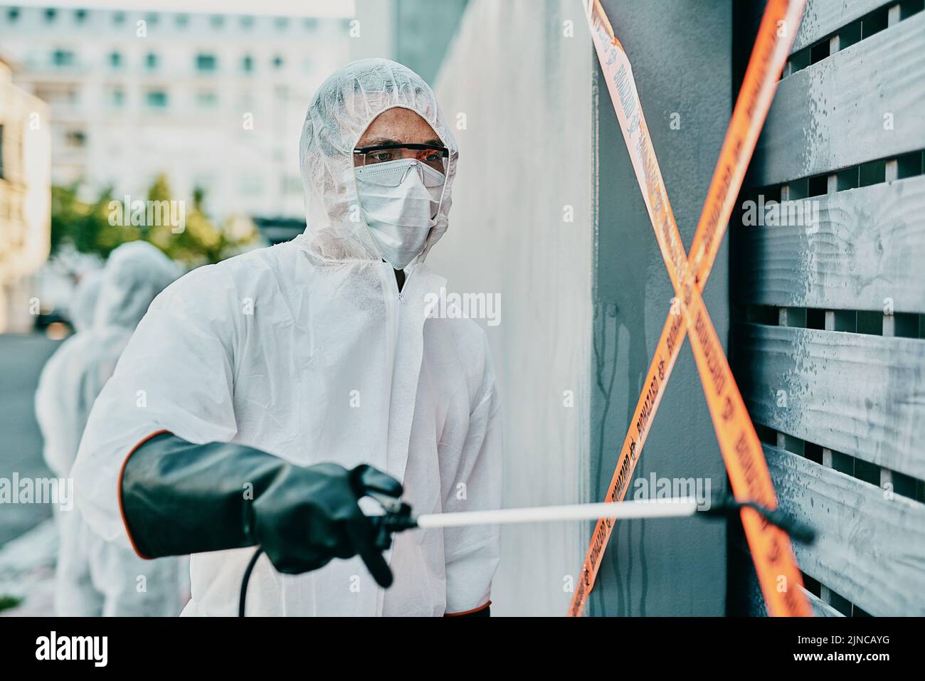 Healthcare worker in covid pandemic, sanitizing and cleaning area with disinfectant, barrier or caution tape and a face mask. Emergency medical person Stock Photo