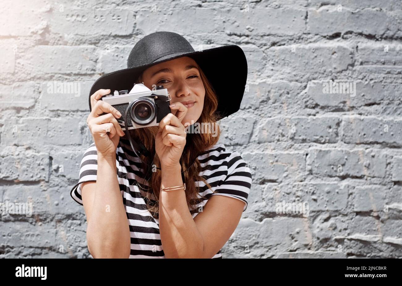 Capturing every moment in the city. a young woman taking a picture with her camera against a brick wall outdoors. Stock Photo