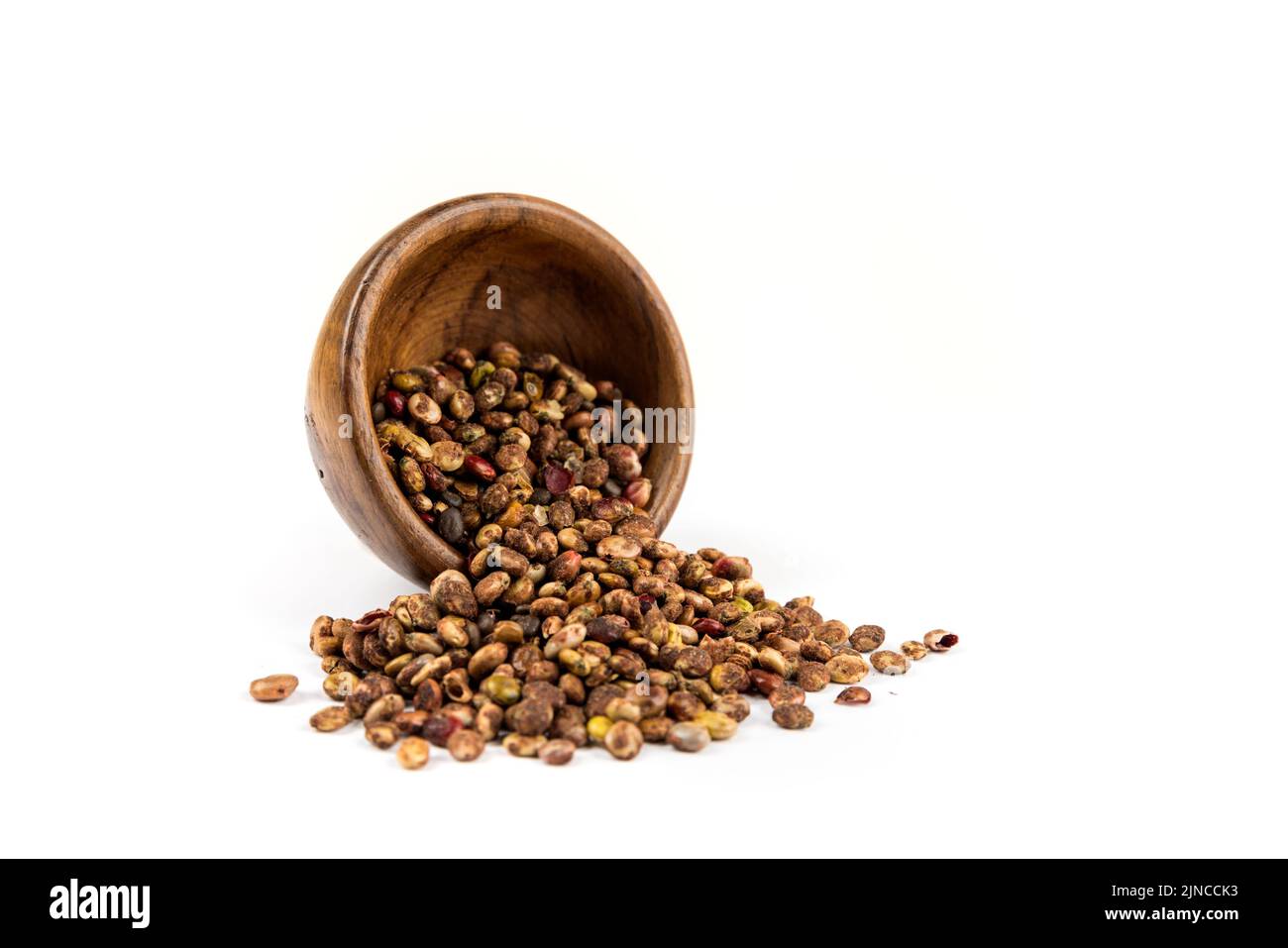 Whole dried sumac berries spilling out of a small wood bowl over white