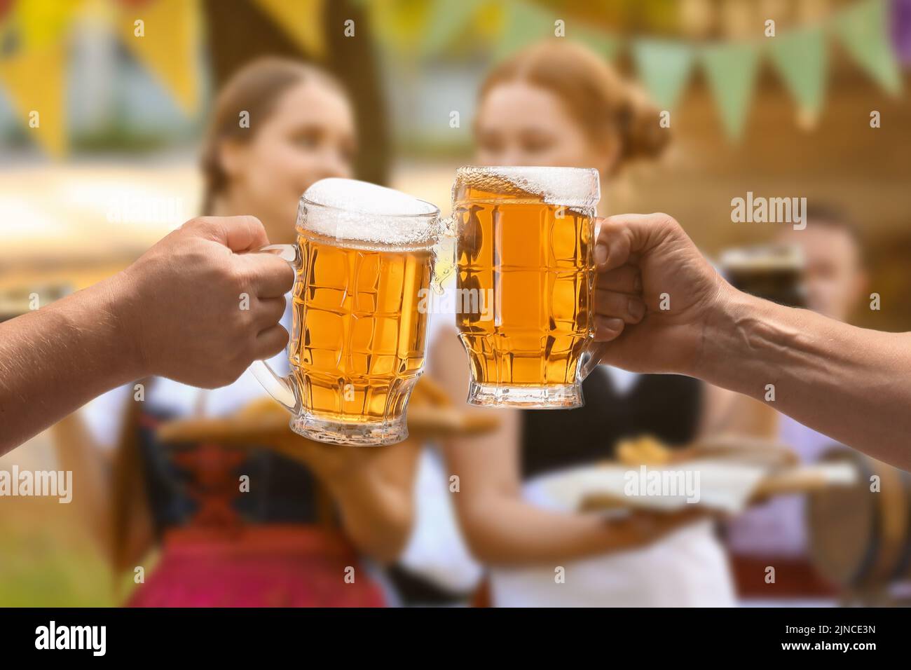 Men clinking mugs with beer during celebration of Octoberfest outdoors Stock Photo