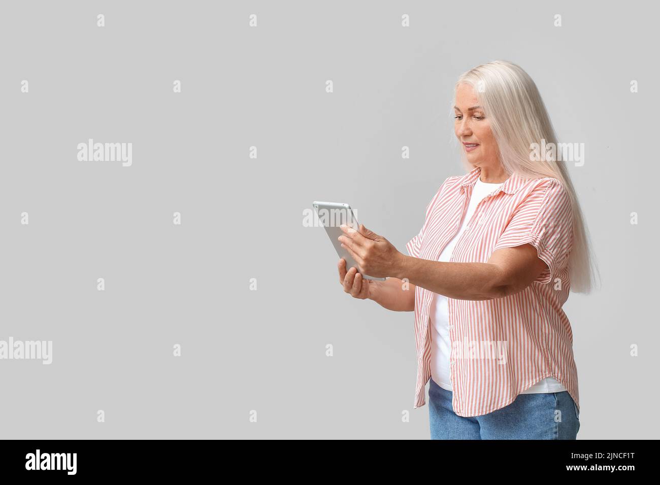 Mature woman using tablet computer for navigation on light background Stock Photo