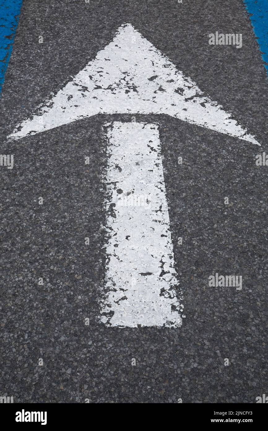 White painted car traffic direction arrow with peeling paint on black asphalt pavement, Montreal, Quebec, Canada Stock Photo