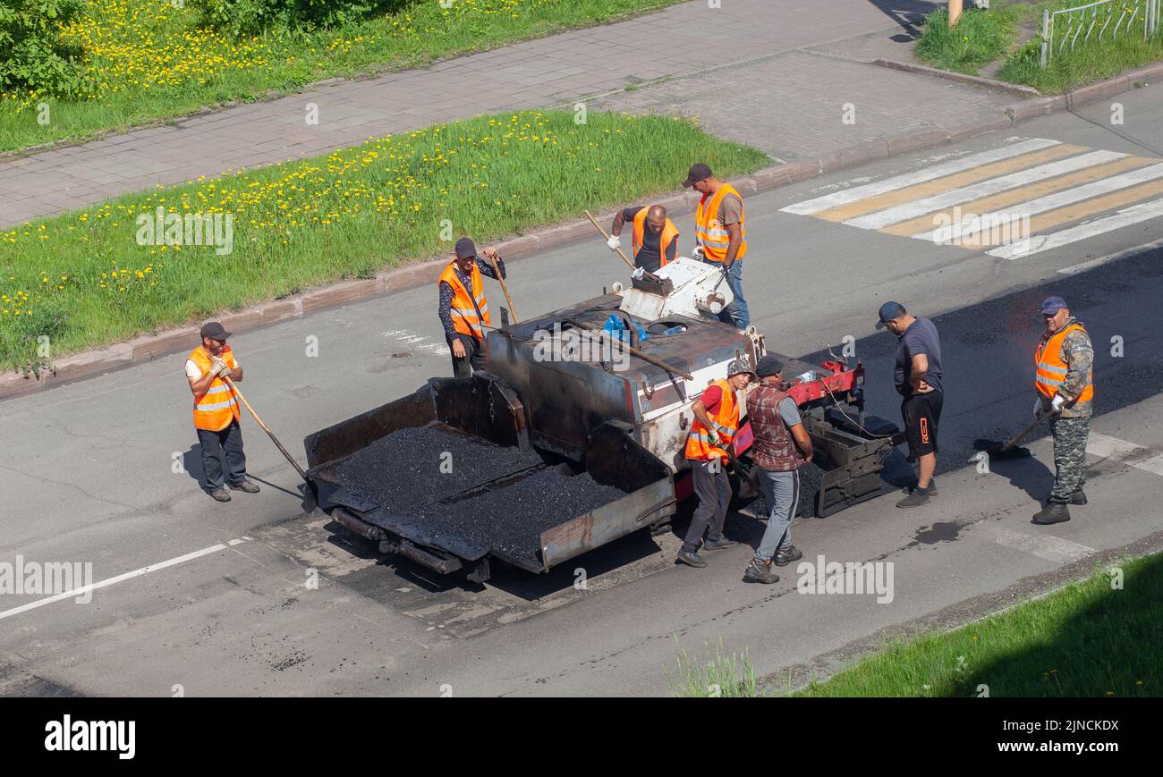 11.06.2022. Kemerovo, Russia. Road works on asphalt laying. Workers in vests are laying patches and rolling them out with a large roller. Stock Photo