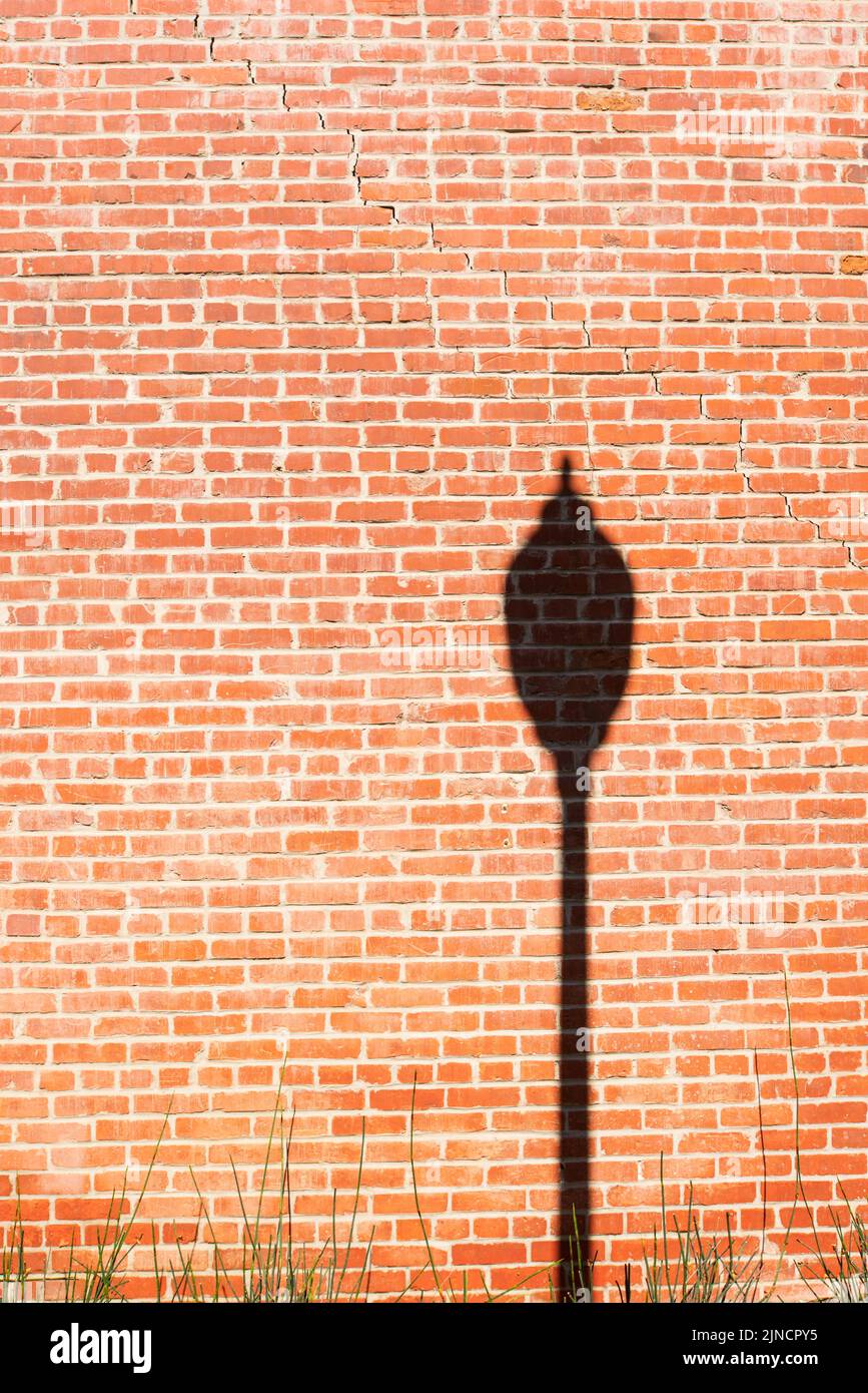 Silhouette of a single street lamp on the right side of a bright blank vertical red brick wall. Stock Photo