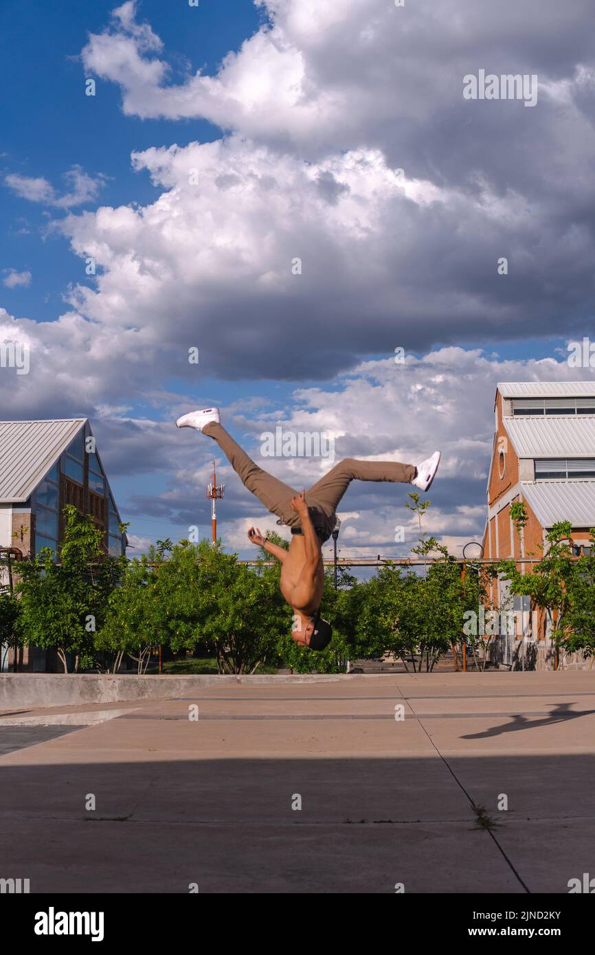 Latino man doing a somersault in mid-air. Hispanic boy doing an extreme flip. Man performing a stunt in the park. Hispanic boy doing an extreme breakd Stock Photo