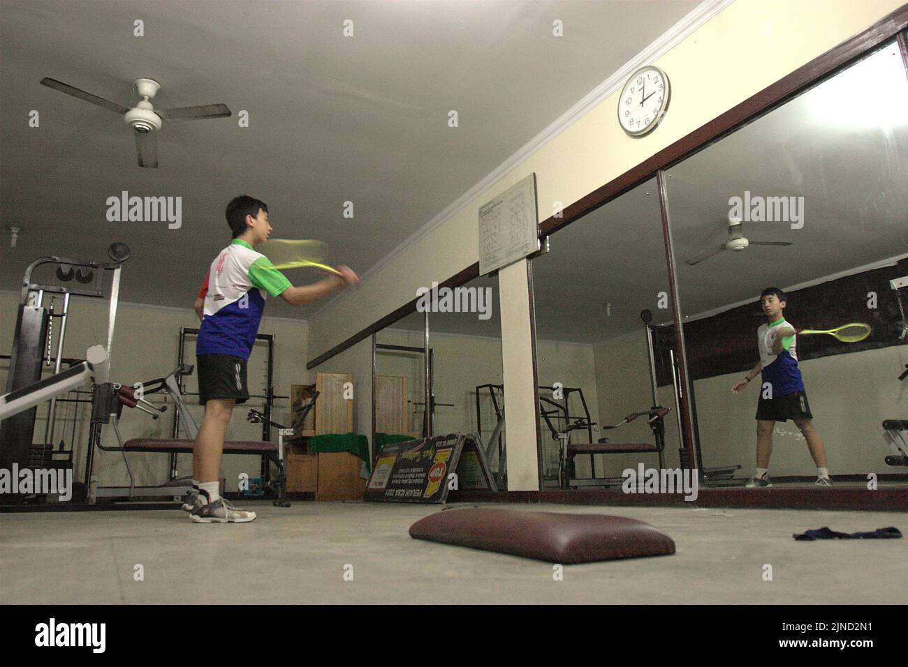 A young badminton athlete is practising various strokes in front of a large mirror at Jaya Raya badminton club in Jakarta, Indonesia. Stock Photo