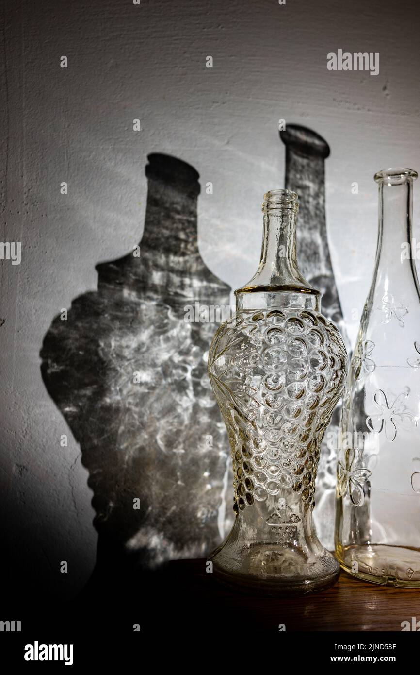 Two transparent vintage bottles and an abstract shadow from them on the wall. Stock Photo