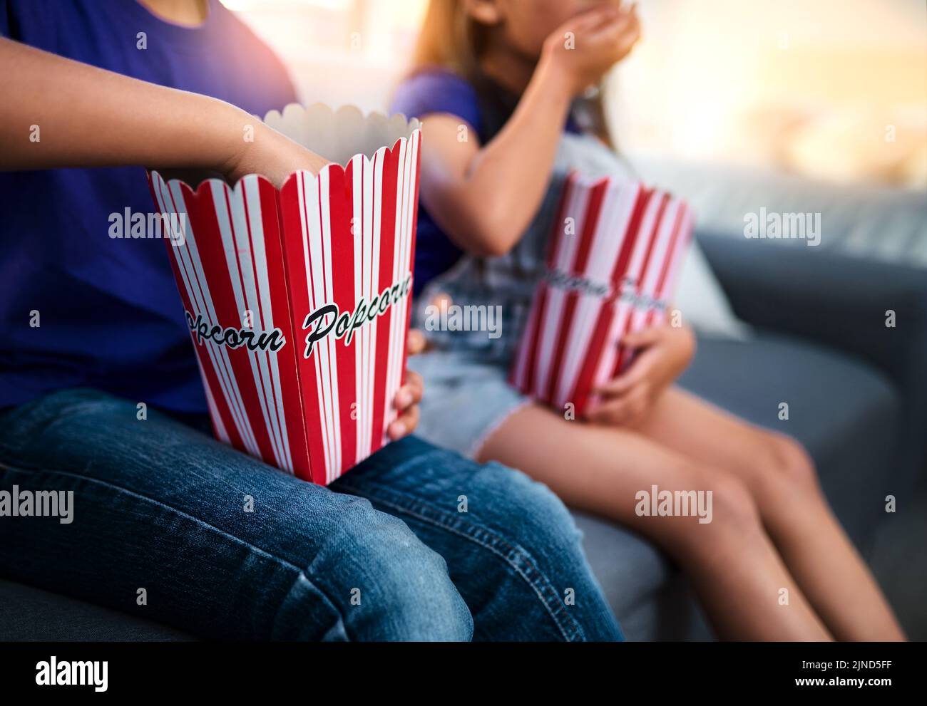 Digging right in. two unrecognizable young children sitting on a sofa and eating popcorn while watching movies at home. Stock Photo