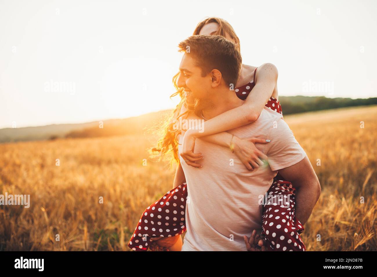 Close-up portrait of a caucasian couple of man and woman walking in an open field, piggy-back ride. Romantic couple dating. Activity relationship. Stock Photo