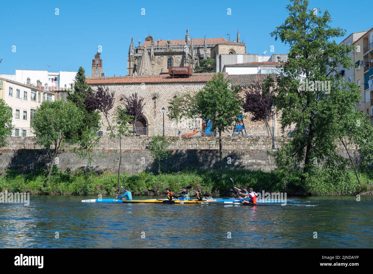 A group or team of young people practices canoeing riding in his canoe navigating the Jerte river and the cathedral in the background Stock Photo