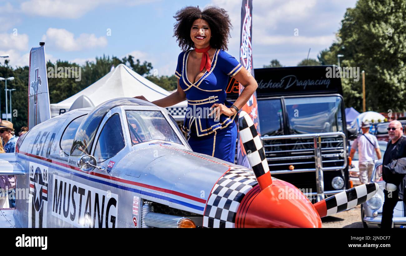 Hannover, Germany, July 23, 2022: Mustang converted from Ford sports car to airplane with smiling pretty young black woman in blue uniform Stock Photo