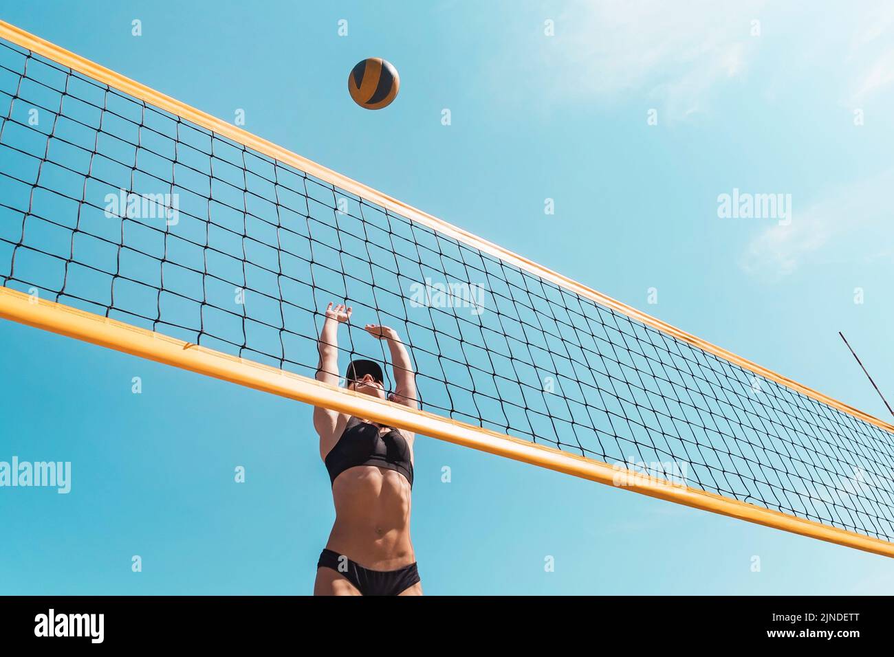 Teenage girl playing beach volleyball. Beach volleyball championship. The woman reaches for the ball. throwing a yellow volleyball over the net. Victo Stock Photo