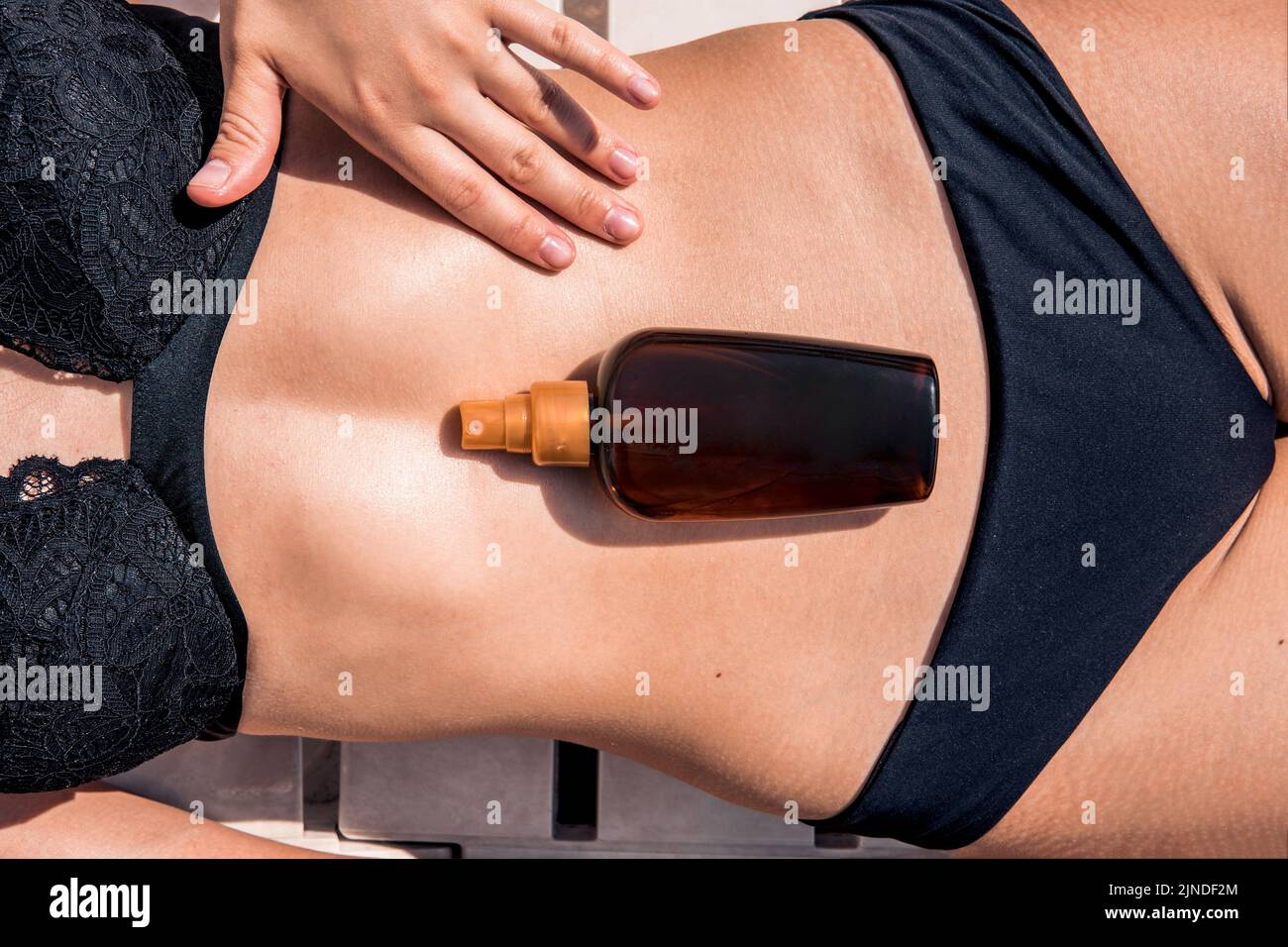 Girl oil spray tanning her legs protection from the sun's uv rays putting sunscreen lotion sunblock. Woman rubs sunscreen into the skin on her stomach Stock Photo