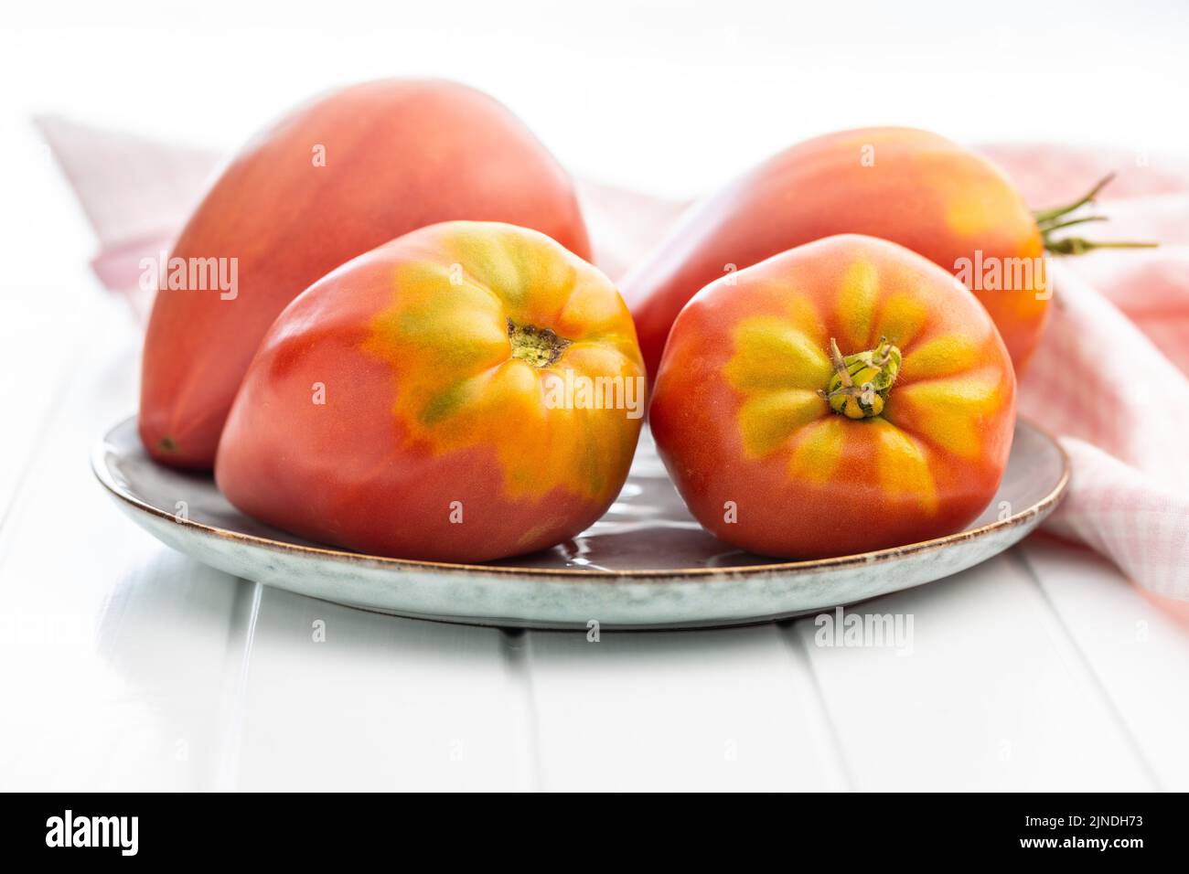 Bull heart tomatoes on plate on a white table. Stock Photo