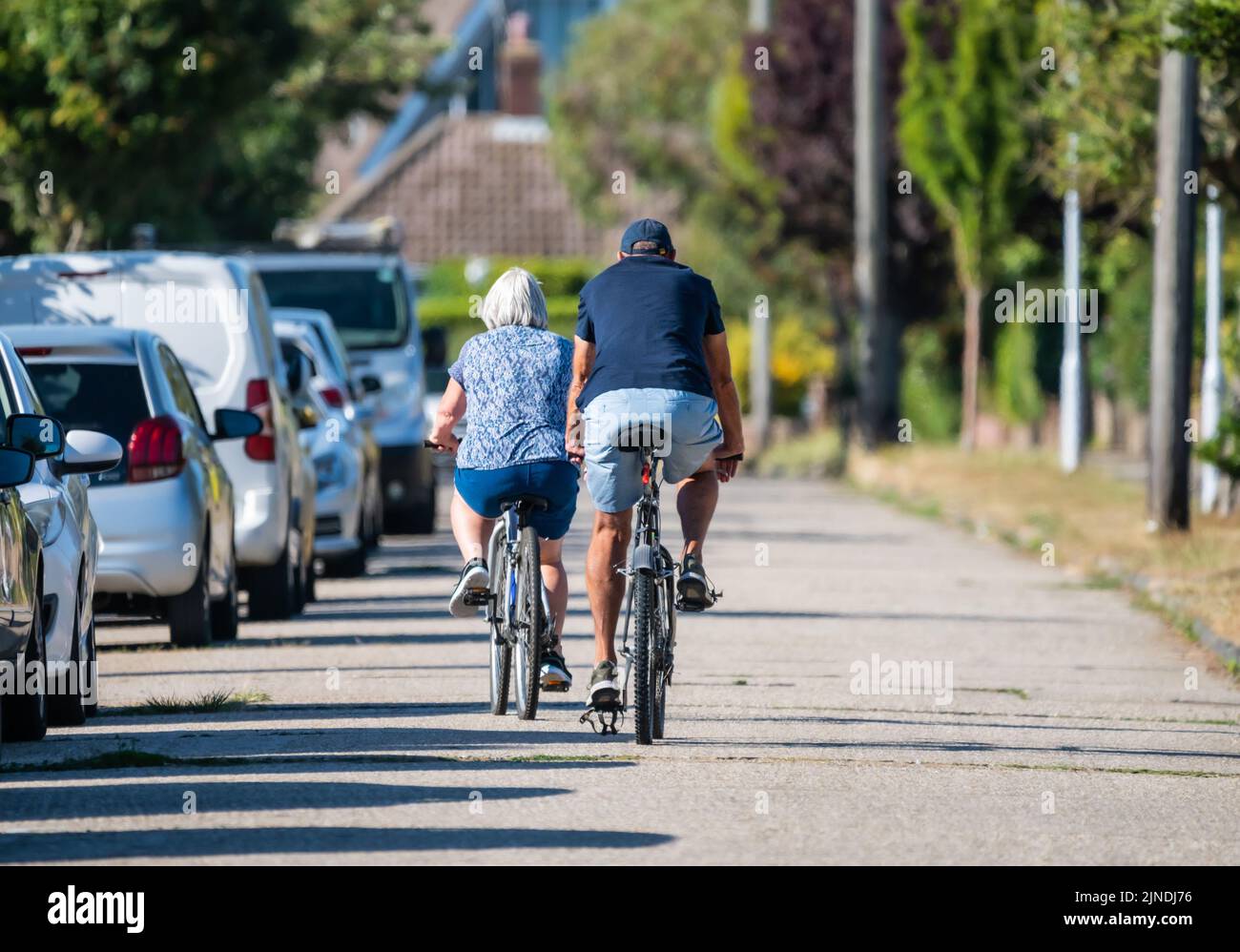 Rear view of a pair of senior cyclists, male & female, riding in the road together on a warm day in Summer, UK. Stock Photo