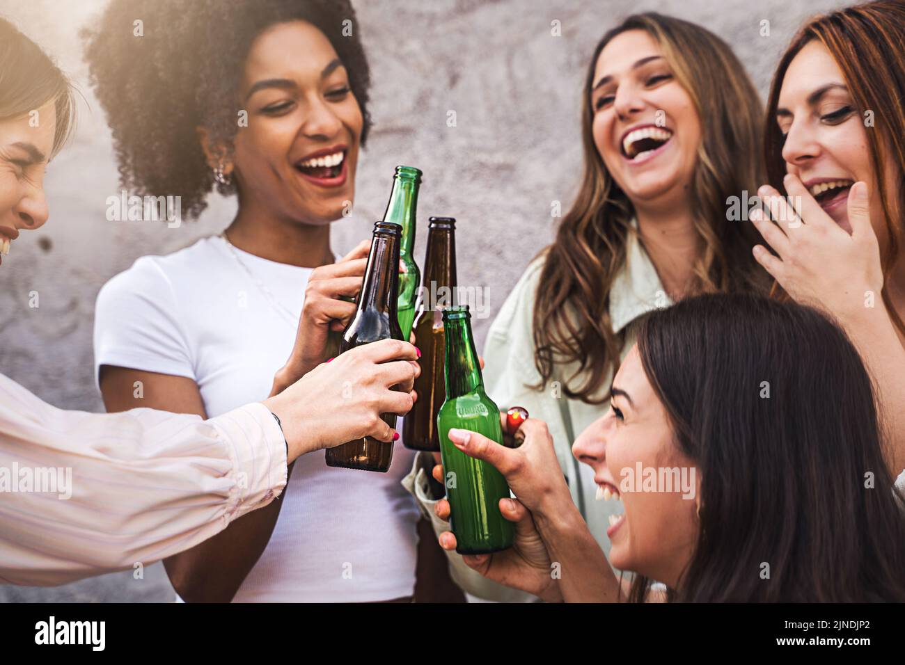 Women only beer party - multiethnic group of cheerful girlfriends having fun toasting and laughing together - focus on the bottles - neutral backgroun Stock Photo