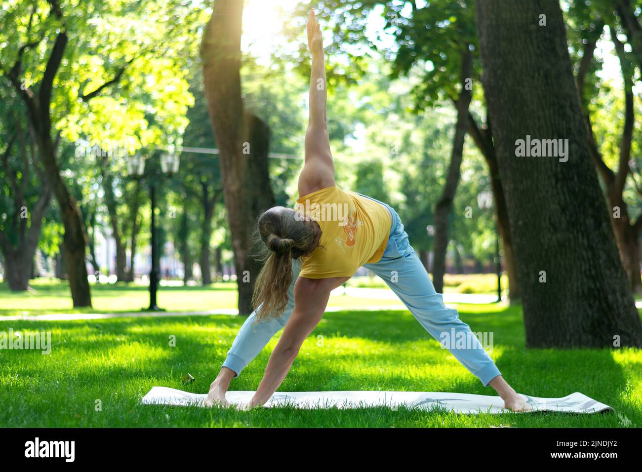 Young man practice yoga in the park. Yoga asanas in city park, sunny day. Concept of meditation, wellbeing and healthy lifestyle Stock Photo