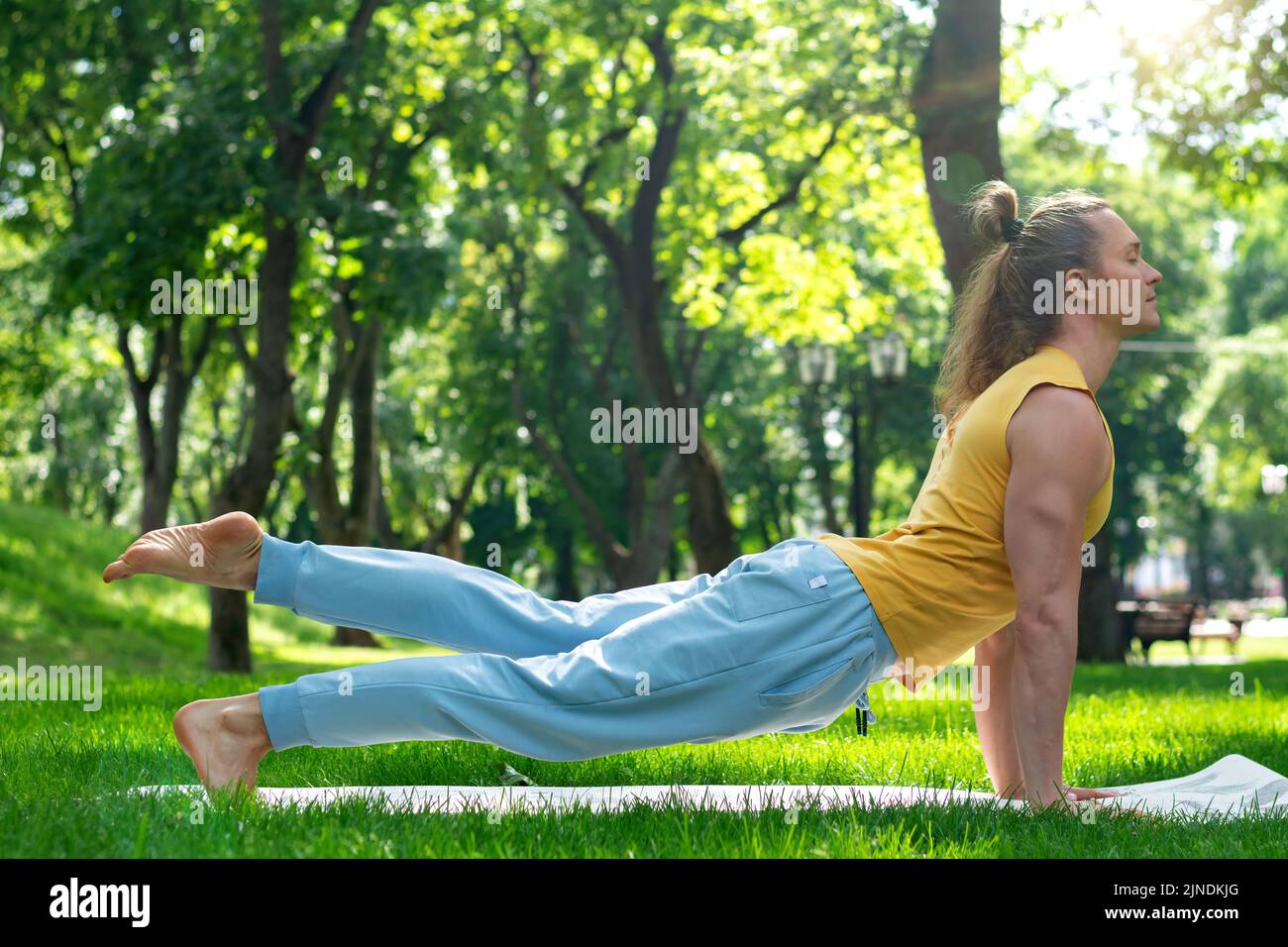 Young man practice yoga in the park. Yoga asanas in city park, sunny day. Concept of meditation, wellbeing and healthy lifestyle Stock Photo