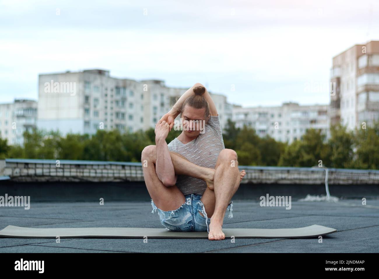 A man practices yoga on the roof of the house. Yoga at sunset. Healthy life, sport and meditation concept. Stock Photo