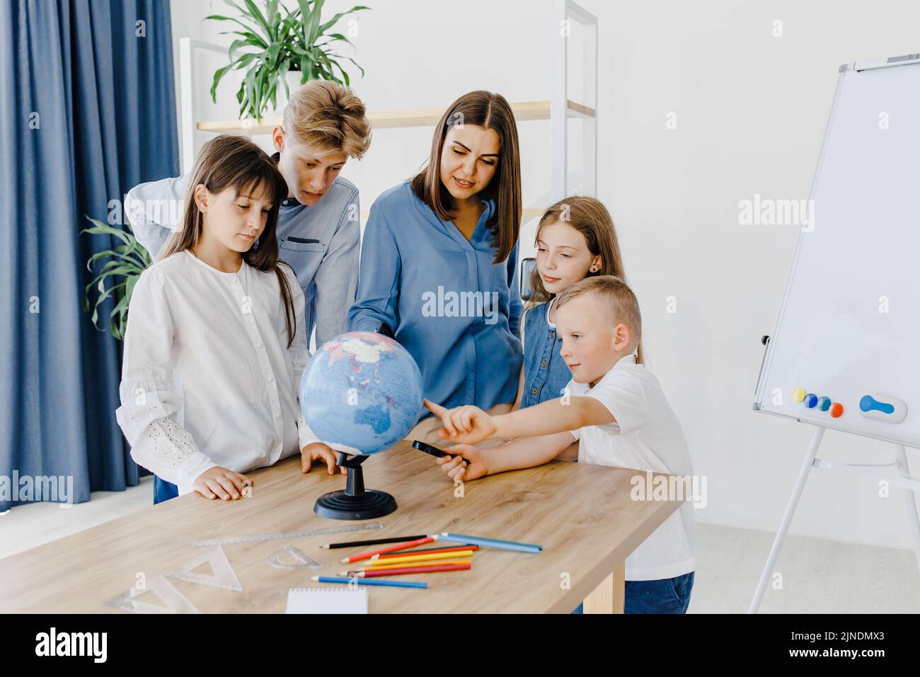 Teacher and children in class are looking at globe, teacher helps explain the lesson to the children in the class at a desk. Educational school proces Stock Photo
