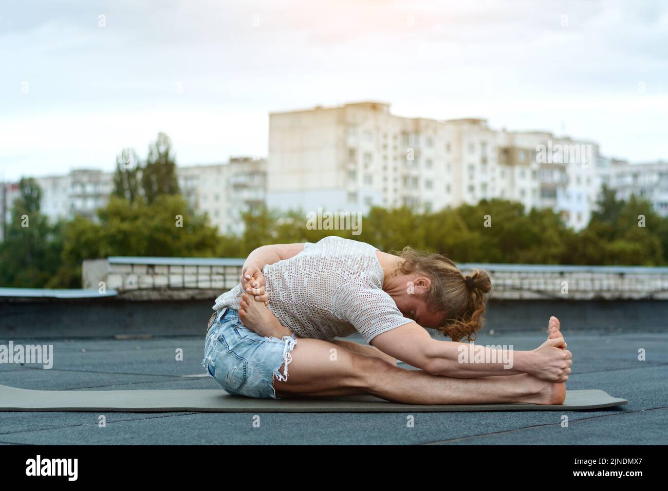 A man practices yoga on the roof of the house. Yoga at sunset. Healthy life, sport and meditation concept. Stock Photo